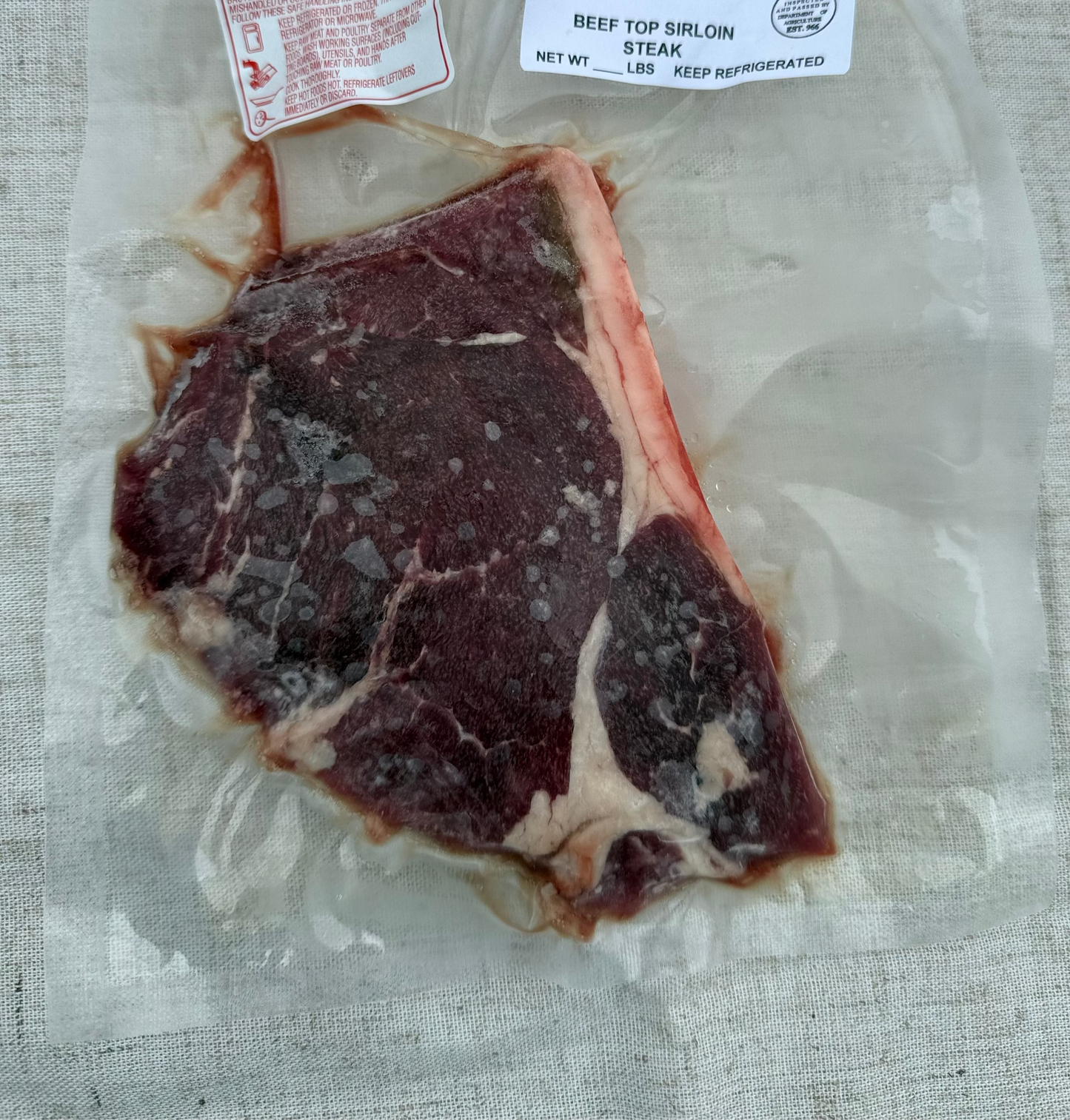 Raw beef top sirloin in a clear plastic bag with labels on a textured surface