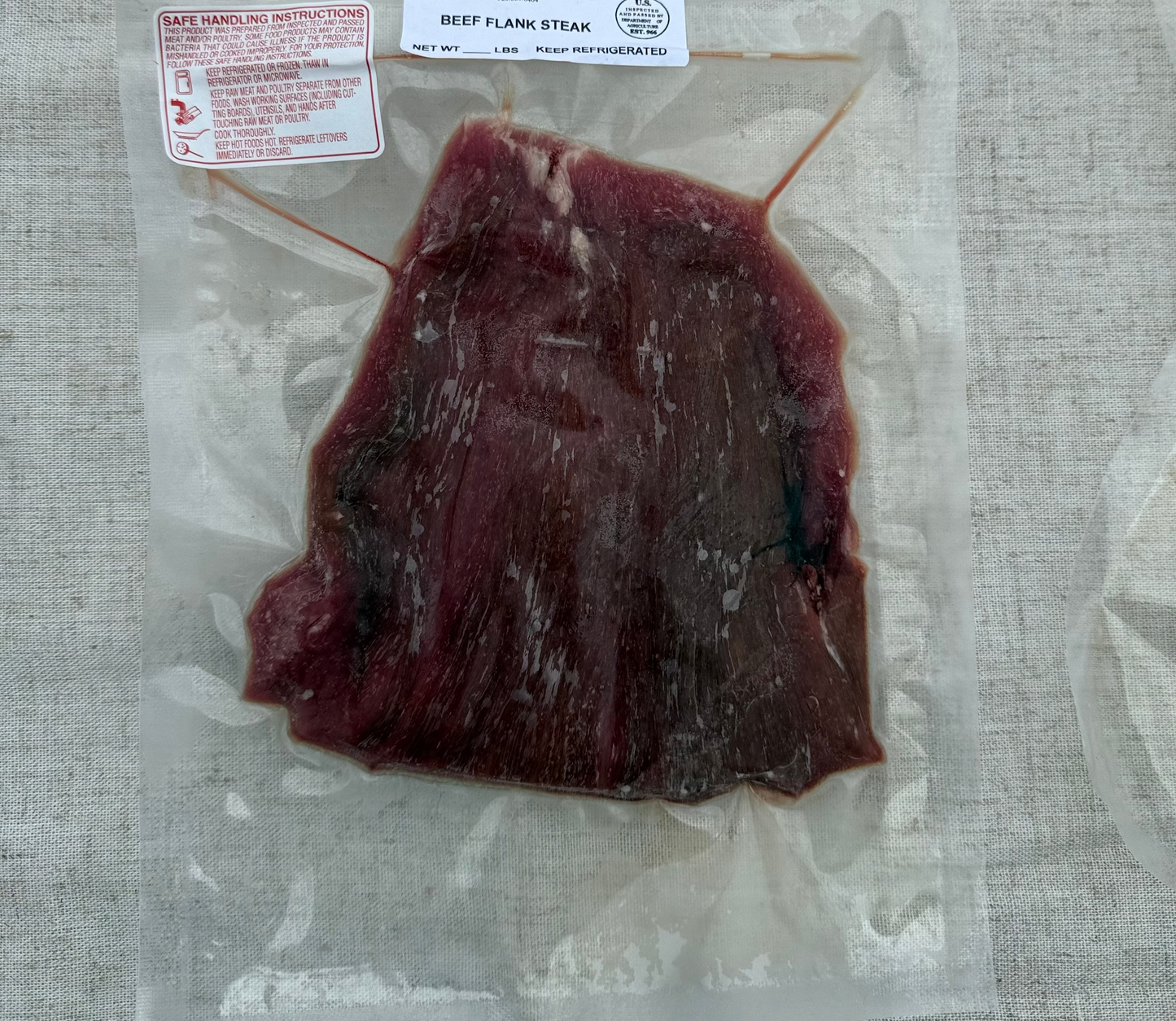Vacuum-sealed beef flank steak with labels on a textured surface
