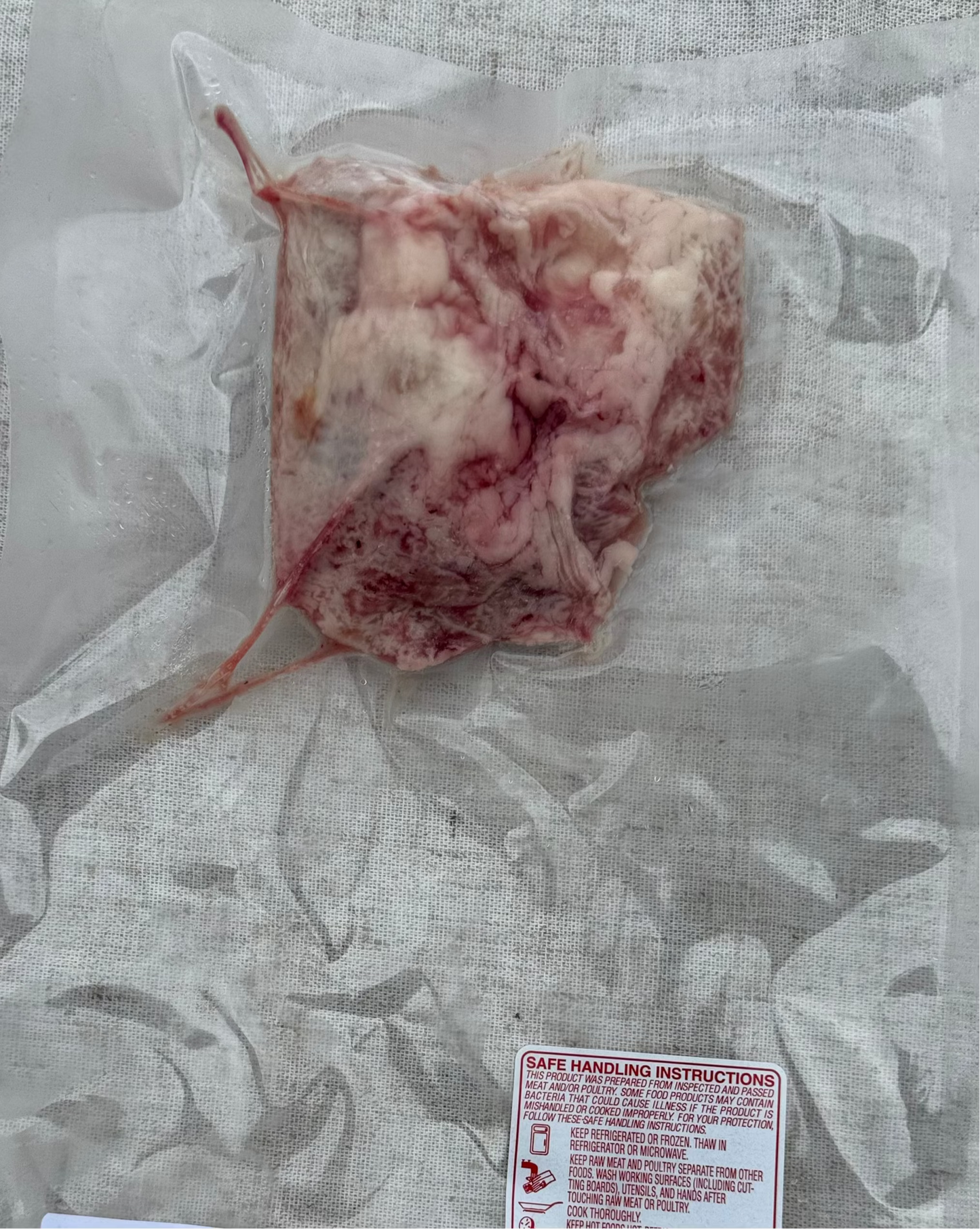 Raw beef sweetbread in a clear plastic packaging on a textured surface