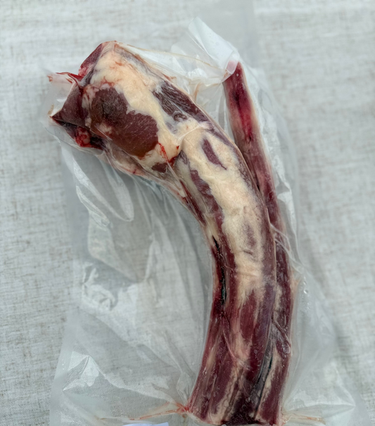 Raw meat rib on clear plastic wrap with a label on a textured surface