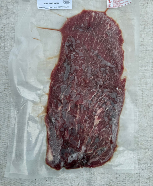Vacuum-sealed beef flat iron steak on a textured surface with labels.