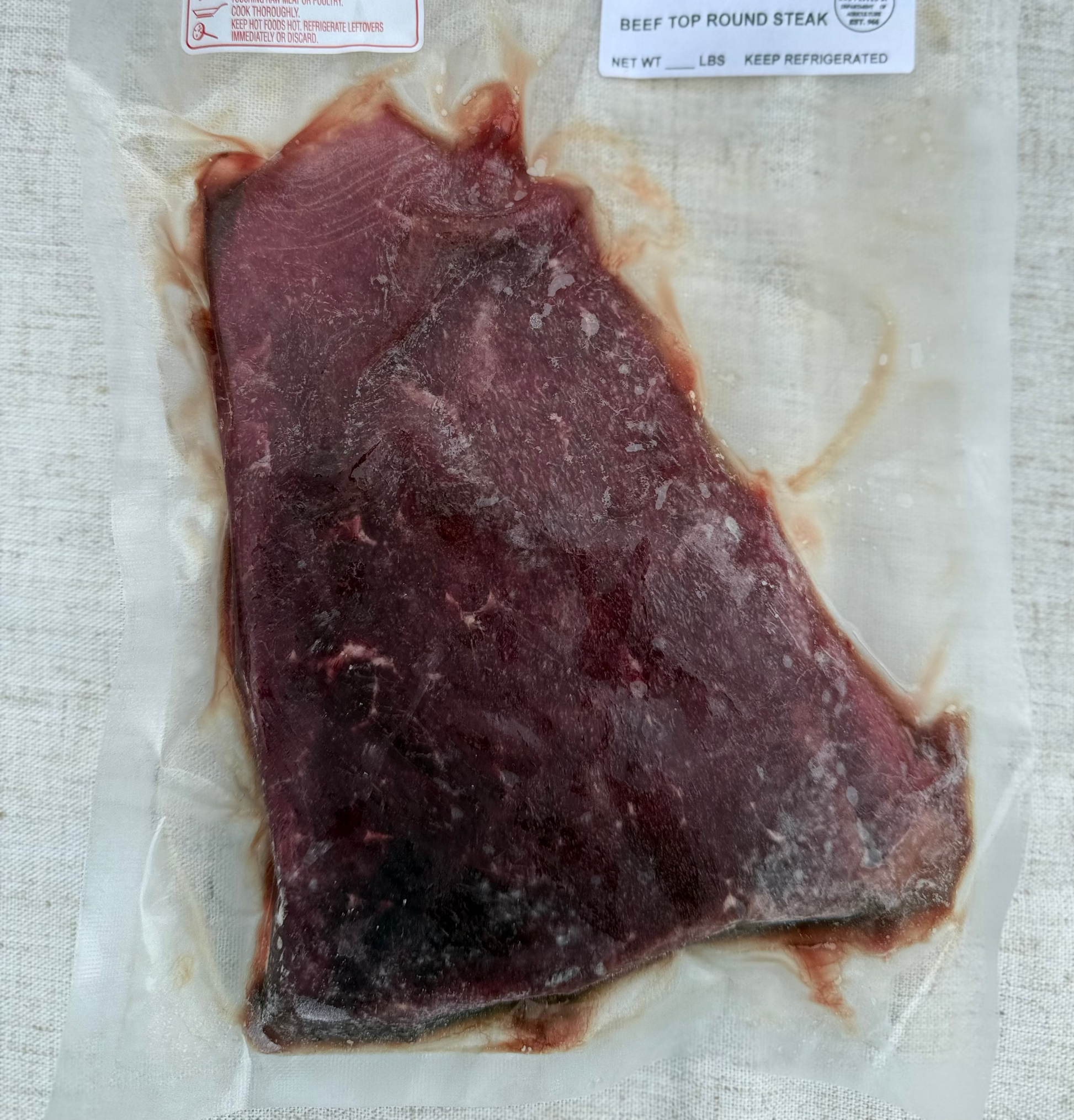 Frozen beef top round steak in packaging with labels on a textured surface