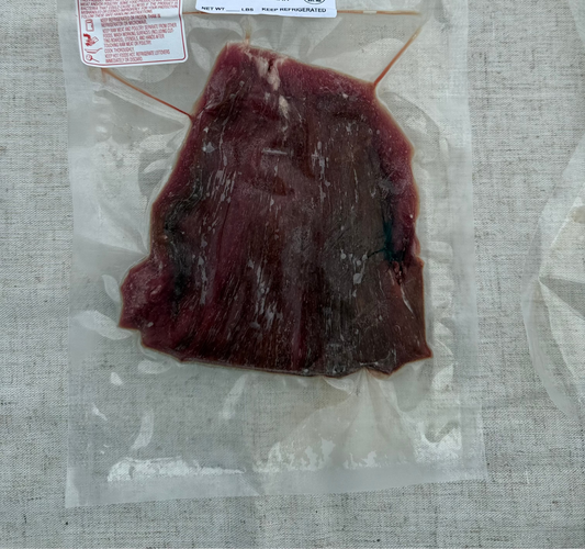 Vacuum-sealed beef flank steak with labels on a textured surface